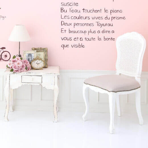 薄いピンクの壁に外国語がオシャレに書かいてあり、白の机と椅子が置かれているスタジオ