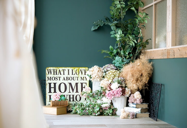 深緑の壁の角に英語の看板やお花・緑の植物・本が飾られているスタジオ